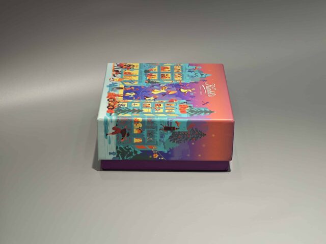 The image showcases a vibrant, customized gift box adorned with lively illustrations of people and animals. It features a unique skincare packaging design, paired with a distinct purple lift-off lid placed nearby.