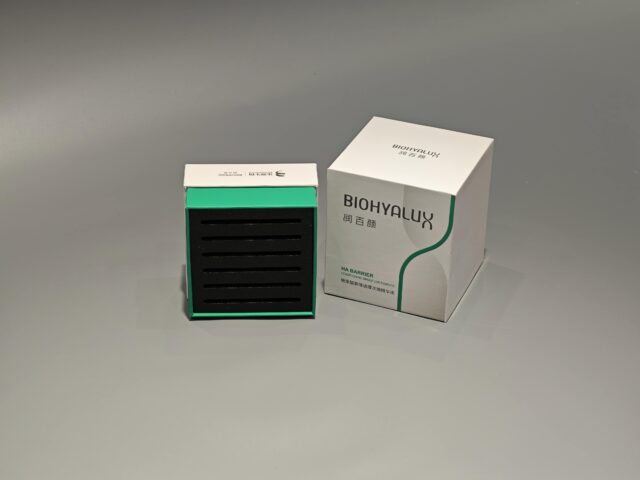 Two custom skincare packaging boxes are stacked on a gray surface, with their lift-off lids slightly ajar. The boxes showcase intricate designs and craftsmanship.