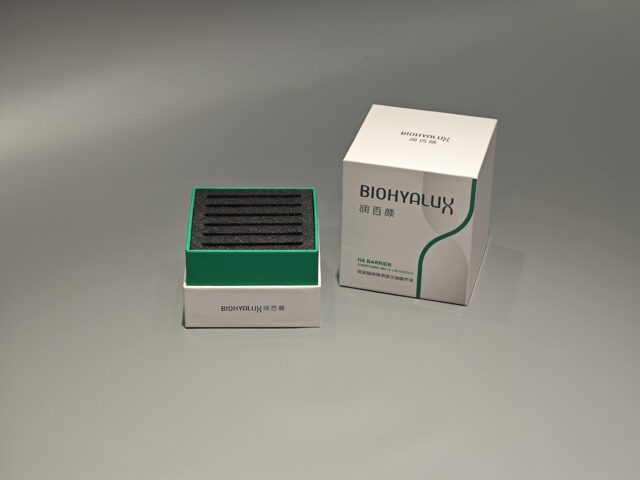 Two custom skincare packaging boxes are stacked on a gray surface, with their lift-off lids slightly ajar. The boxes showcase intricate designs and craftsmanship.