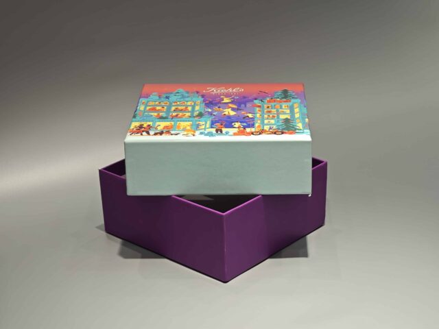 The image showcases a vibrant, customized gift box adorned with lively illustrations of people and animals. It features a unique skincare packaging design, paired with a distinct purple lift-off lid placed nearby.