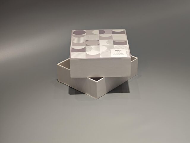 A custom packaging box with a lift-off lid, showcasing an intricate pattern, is displayed elegantly