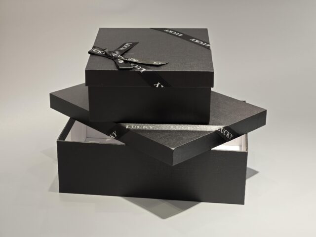 A sleek, custom gift box featuring a dark lift-off lid is elegantly wrapped in a branded ribbon designed with a sophisticated pattern.
