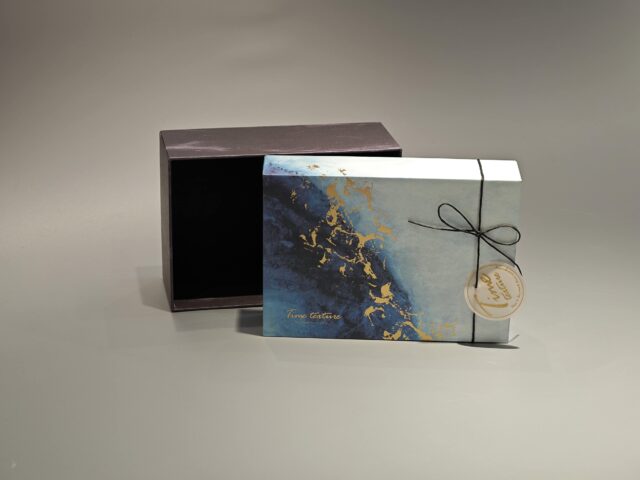 This custom ribbon box showcases a striking blue and gold abstract pattern. Designed with a lift-off lid, it is elegantly finished with a black cord and includes a round tag for added personalization.