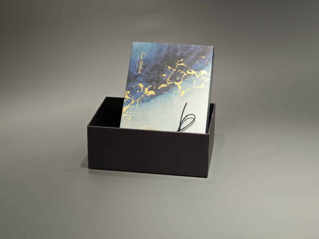 This custom ribbon box showcases a striking blue and gold abstract pattern. Designed with a lift-off lid, it is elegantly finished with a black cord and includes a round tag for added personalization.