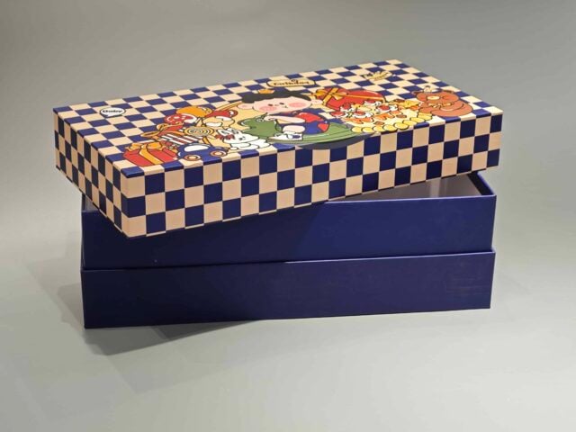 This custom packaging box showcases playful cartoon characters, including a cheerful pig and a chicken, surrounded by a delightful assortment of pastries. The vibrant design is set against an imaginative checkered backdrop, creating an eye-catching presentation for any gift.
