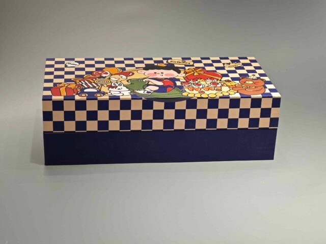 This custom packaging box showcases playful cartoon characters, including a cheerful pig and a chicken, surrounded by a delightful assortment of pastries. The vibrant design is set against an imaginative checkered backdrop, creating an eye-catching presentation for any gift.