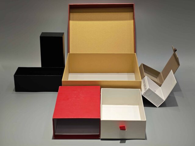 The image showcases a vibrant red and yellow custom packaging solution, featuring an open gift box that reveals a bespoke red rigid box and an included flat package.