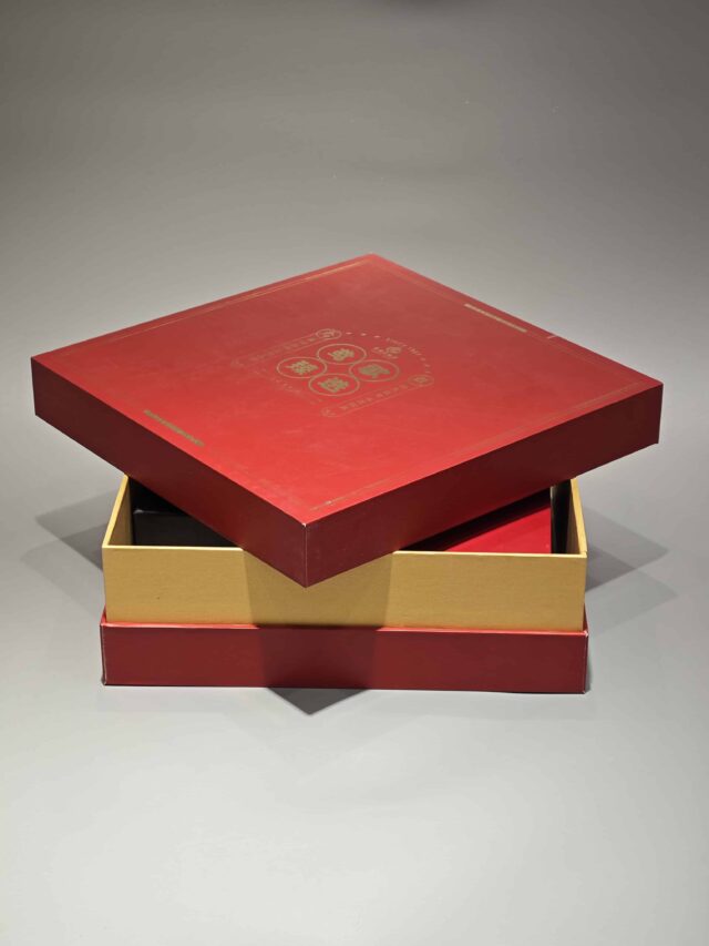 The image showcases a vibrant red and yellow custom packaging solution, featuring an open gift box that reveals a bespoke red rigid box and an included flat package.