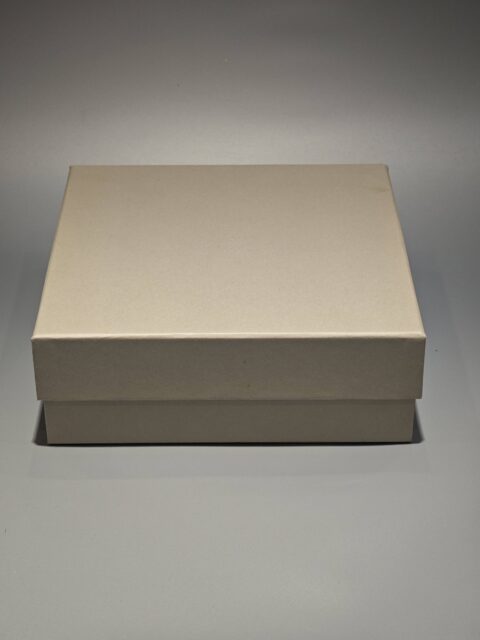 A custom square rigid box with a removable top positioned slightly ajar on the side, set against a neutral backdrop.