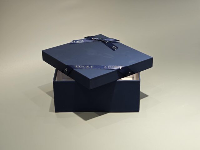 A sleek, custom gift box featuring a dark lift-off lid is elegantly wrapped in a branded ribbon designed with a sophisticated pattern.