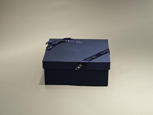 A sleek, custom gift box featuring a dark lift-off lid is elegantly wrapped in a branded ribbon designed with a sophisticated pattern.