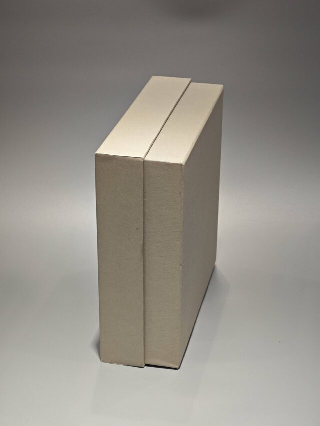 A custom square rigid box with a removable top positioned slightly ajar on the side, set against a neutral backdrop.