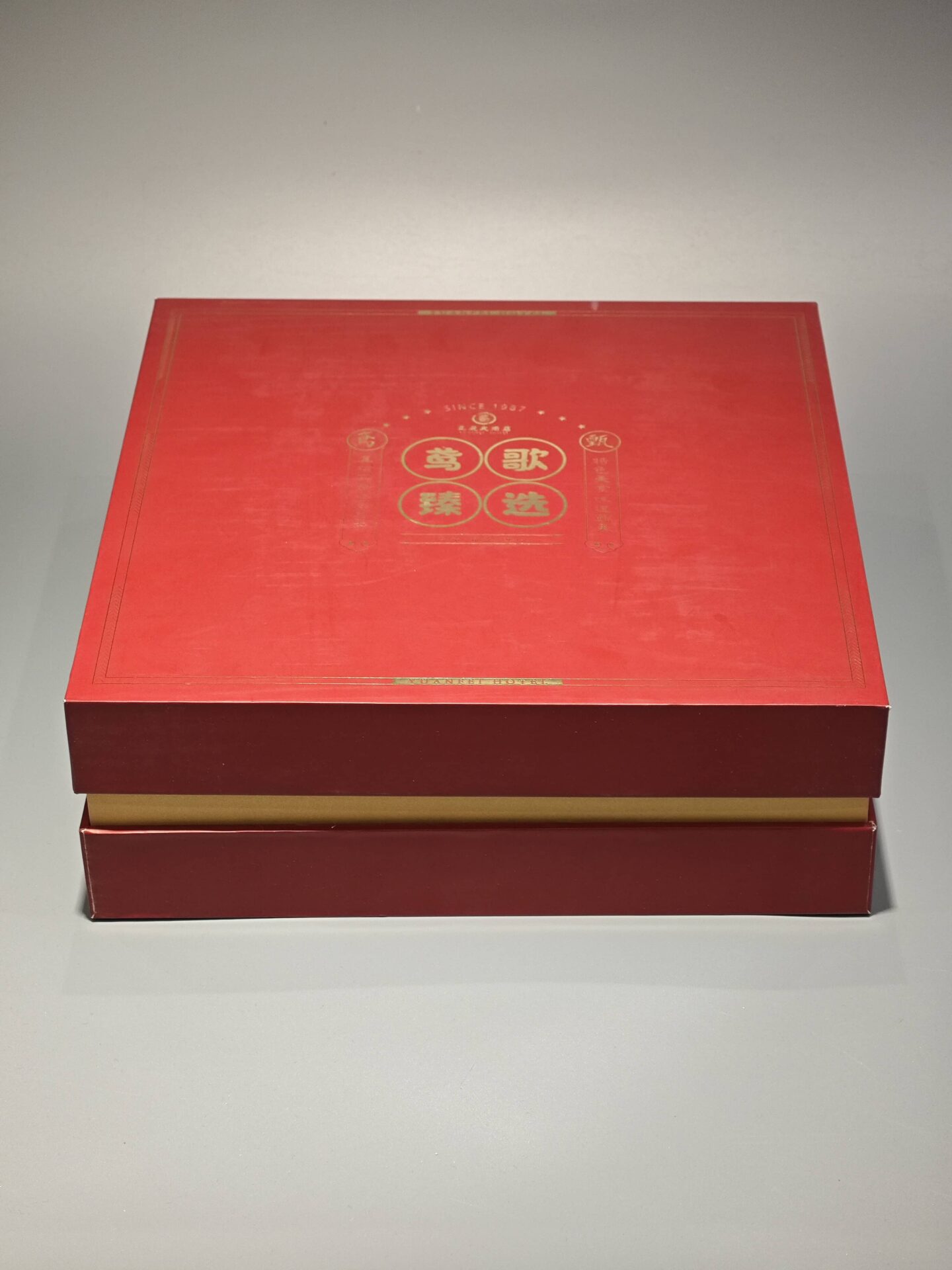 The image showcases a vibrant red and yellow custom packaging solution, featuring an open gift box that reveals a bespoke red rigid box and an included flat package.
