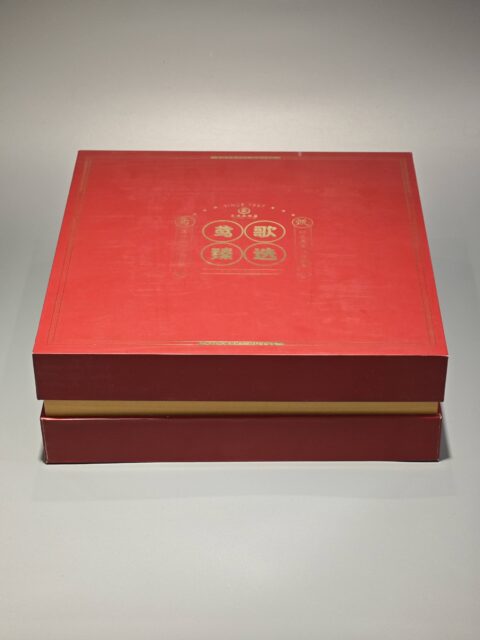 The image showcases a vibrant red and yellow custom packaging solution, featuring an open gift box that reveals a bespoke red rigid box and an included flat package.