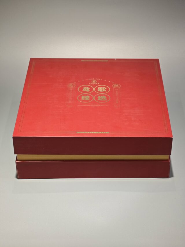 The image showcases a vibrant red and yellow custom packaging solution, featuring an open gift box that reveals a bespoke red rigid box and an included flat package.