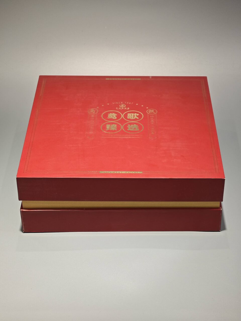 The image showcases a vibrant red and yellow custom packaging solution, featuring an open gift box that reveals a bespoke red rigid box and an included flat package.