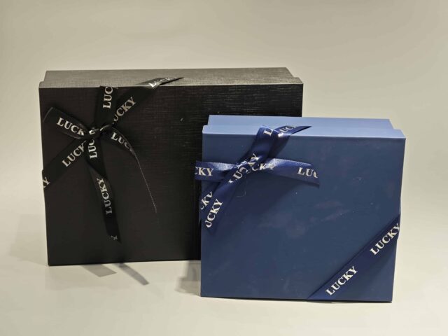 A sleek, custom gift box featuring a dark lift-off lid is elegantly wrapped in a branded ribbon designed with a sophisticated pattern.