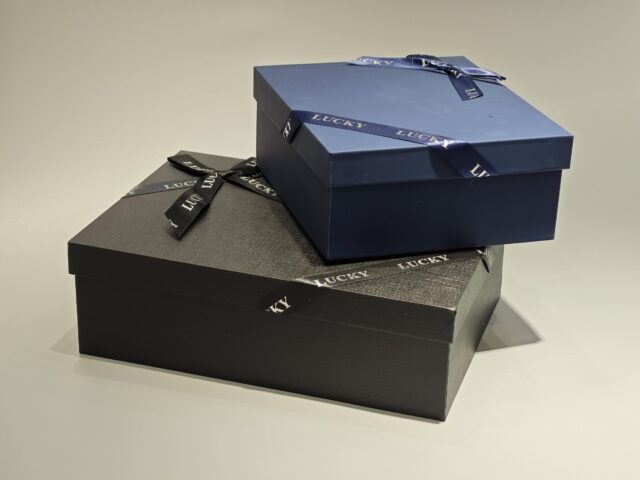 A sleek, custom gift box featuring a dark lift-off lid is elegantly wrapped in a branded ribbon designed with a sophisticated pattern.