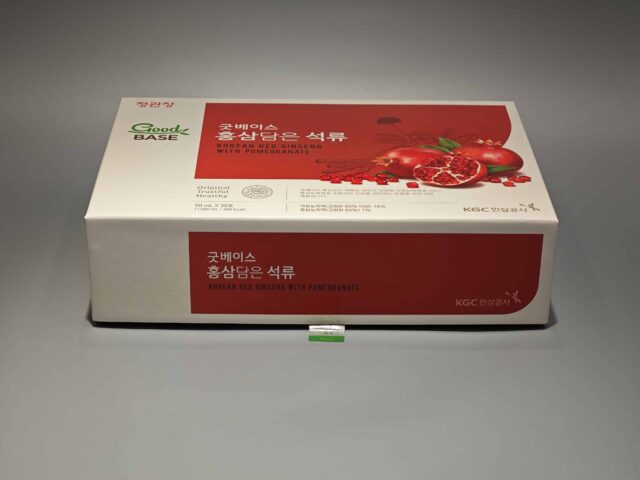 The product is a custom box packaging for a Korean Red Ginseng with Pomegranate product. The box features vibrant and detailed illustrations of ginseng roots and pomegranate fruits, giving it an appealing and eye-catching design. The overall color scheme complements the images, set against a gray surface that enhances the vividness of the artwork. This bespoke packaging highlights both traditional and contemporary aesthetics, reflecting the premium quality of its contents.