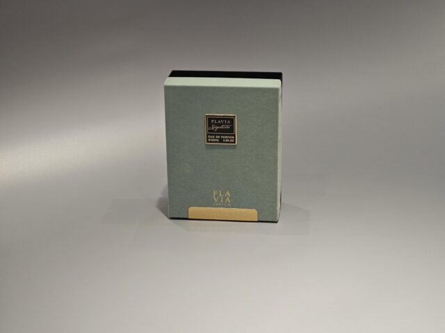 The image showcases two exquisite custom packaging boxes for Flavia perfume. One box features a light green design with silver accents, while the other is dark green with gold accents, both incorporating elegant foil stamping details.