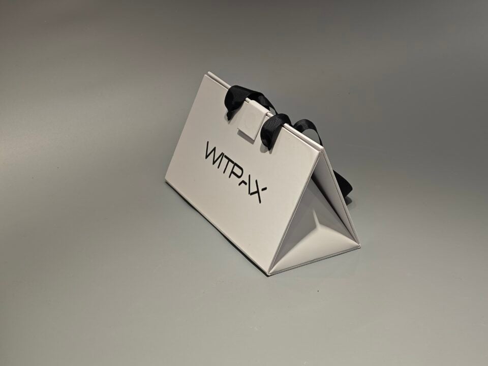 The custom collapsible packaging box, crafted from white cardboard and featuring sleek black handles, sits elegantly on a light gray surface, exemplifying sophisticated design.